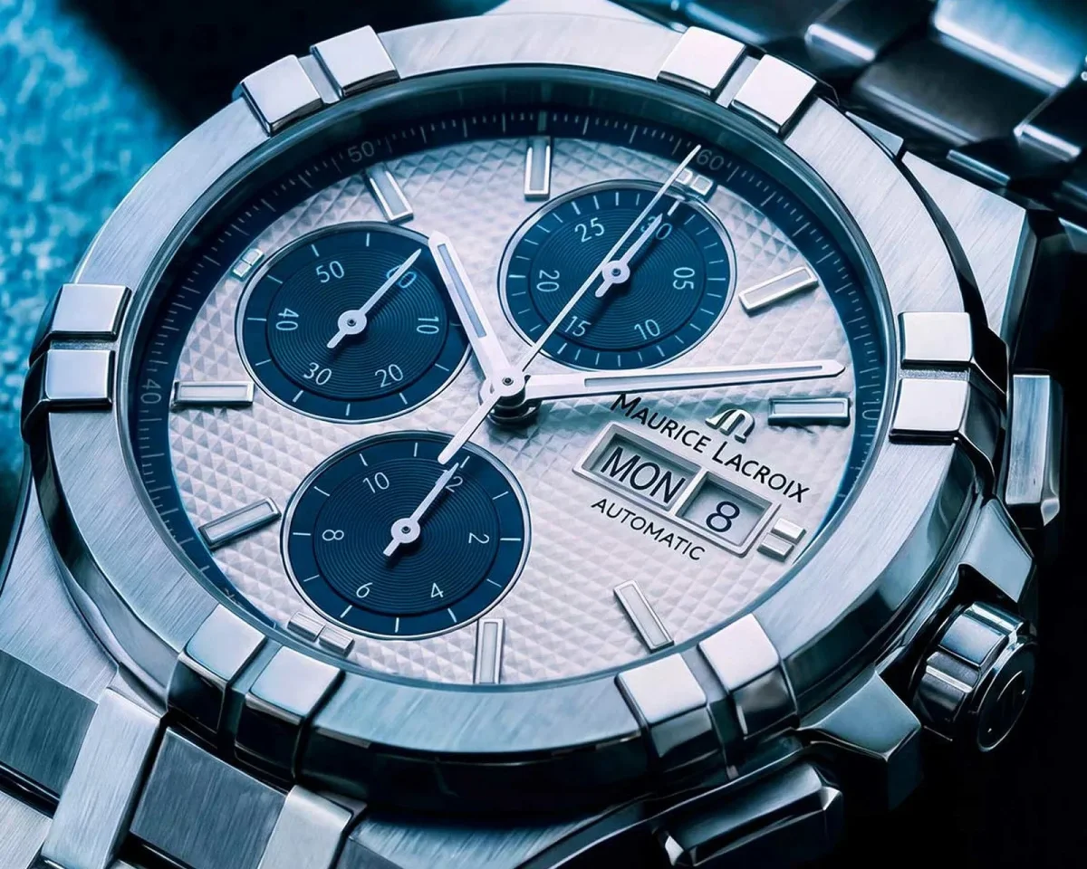 Maurice Lacroix automatic chronograph watch featuring a silver textured dial, three blue sub-dials, and a day-date window, presented on a silver metal bracelet.