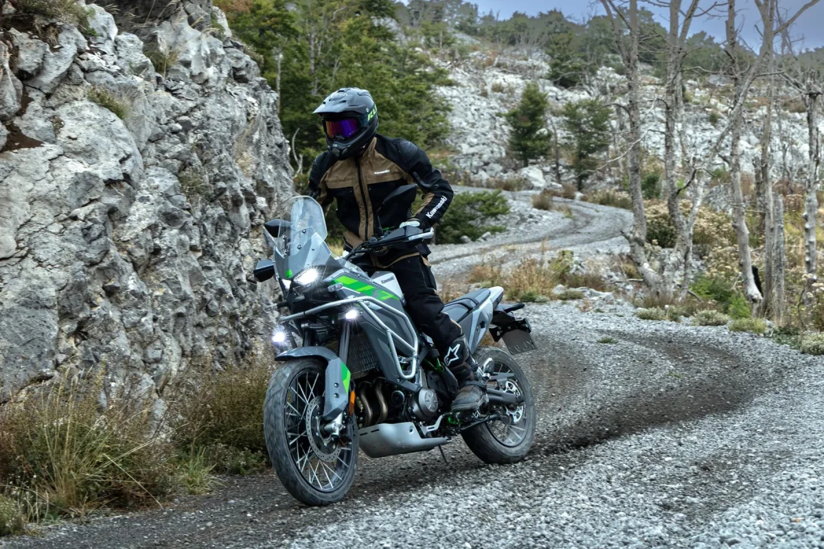Kawasaki motorcycle traveling along a narrow, winding gravel road through a rocky landscape.