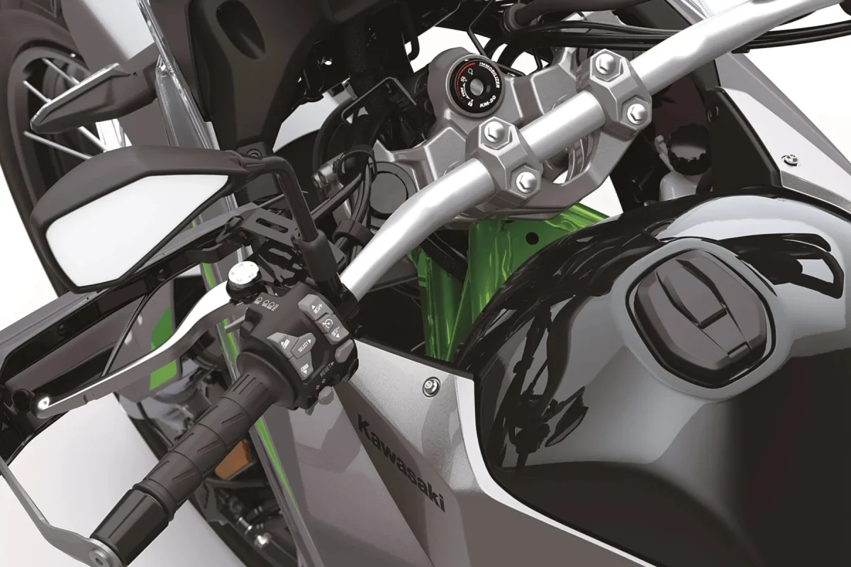 Close-up of the handlebars, ignition, and fuel tank of a grey and green Kawasaki motorcycle.