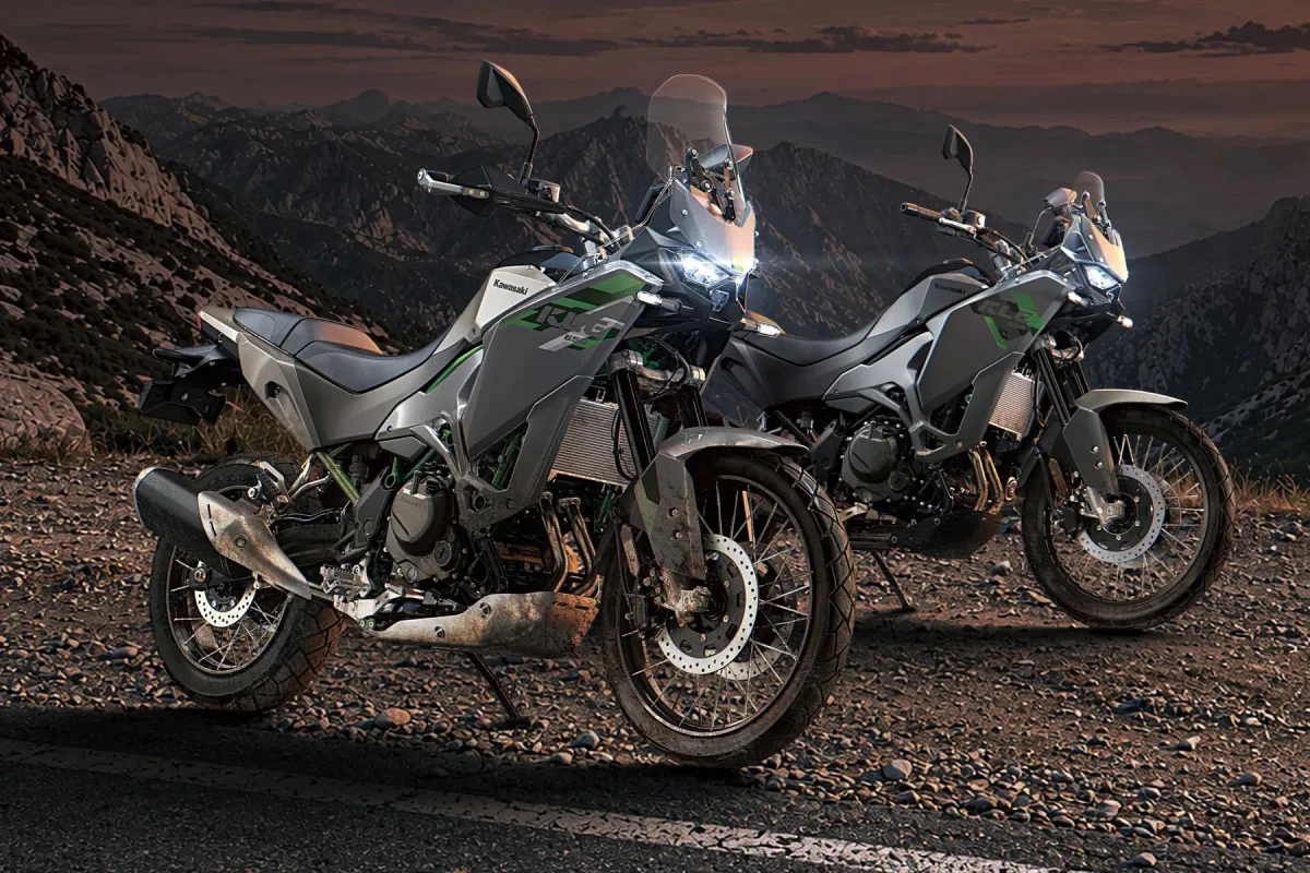 Two gray Kawasaki KLR650 adventure motorcycles parked on a rocky mountain path at dusk.