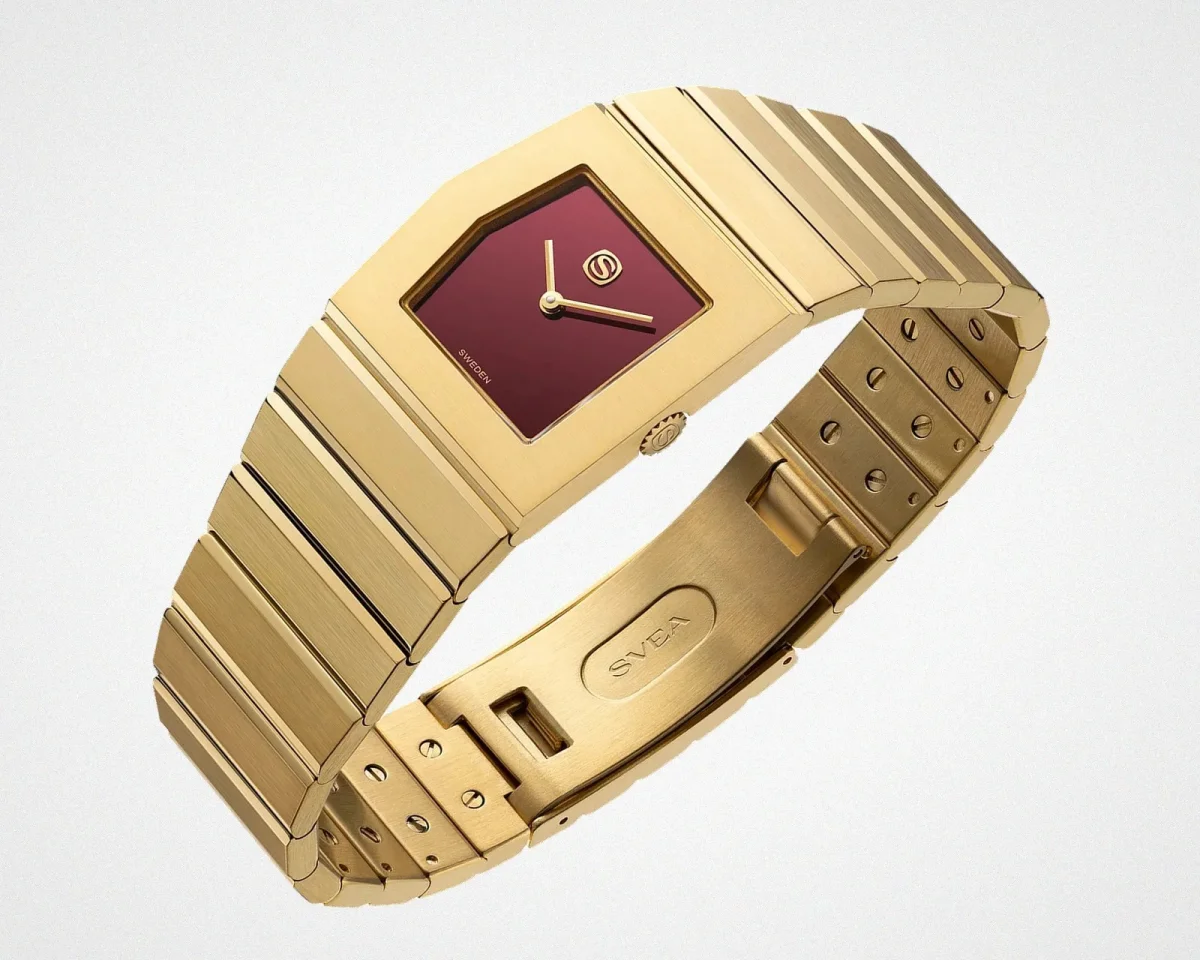 Gold-tone metal watch with a rectangular burgundy dial, gold hands, and a segmented link bracelet featuring an engraved SVEA logo on the clasp.