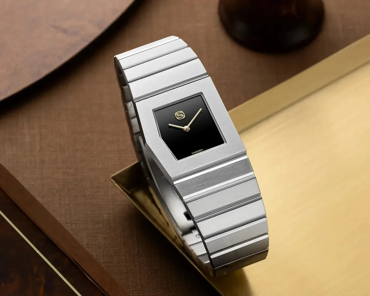 Silver-toned wristwatch featuring a rectangular black face, gold hands, and a linked metal bracelet.