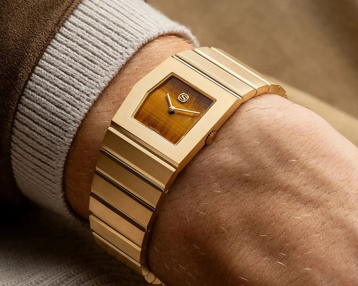 Gold-tone watch with an integrated link bracelet and a rectangular dial featuring a striped brown inlay.