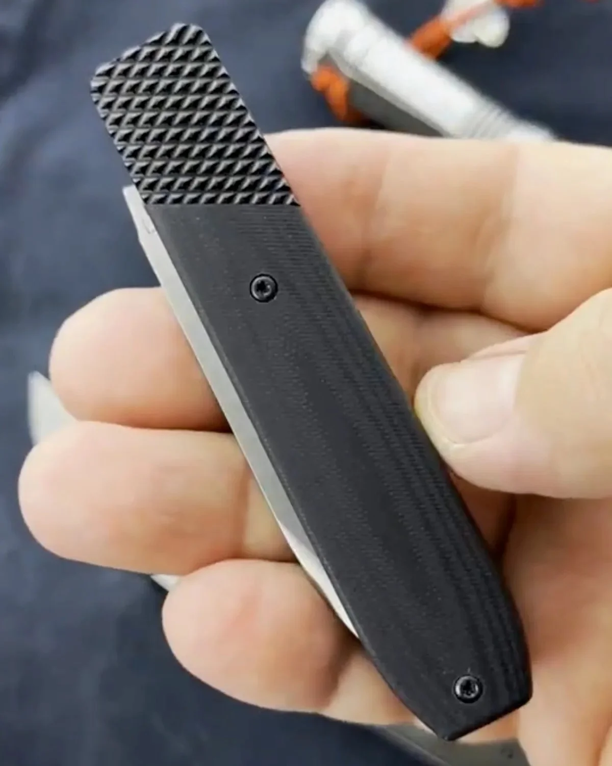Black folding knife with a textured, diamond-patterned handle held in a hand.