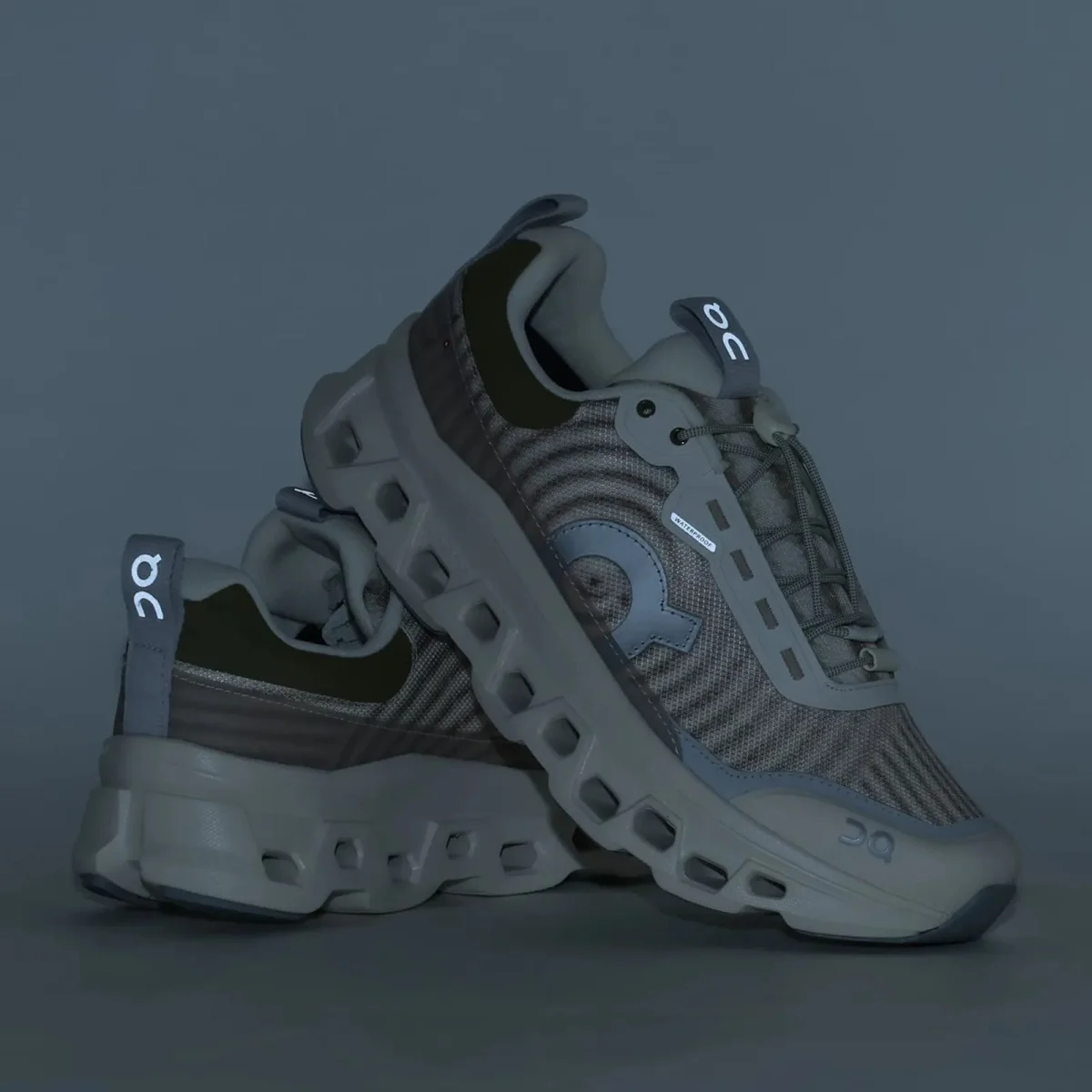 On Running waterproof sneaker in light olive and grey featuring reflective logo details and a chunky, cushioned sole.