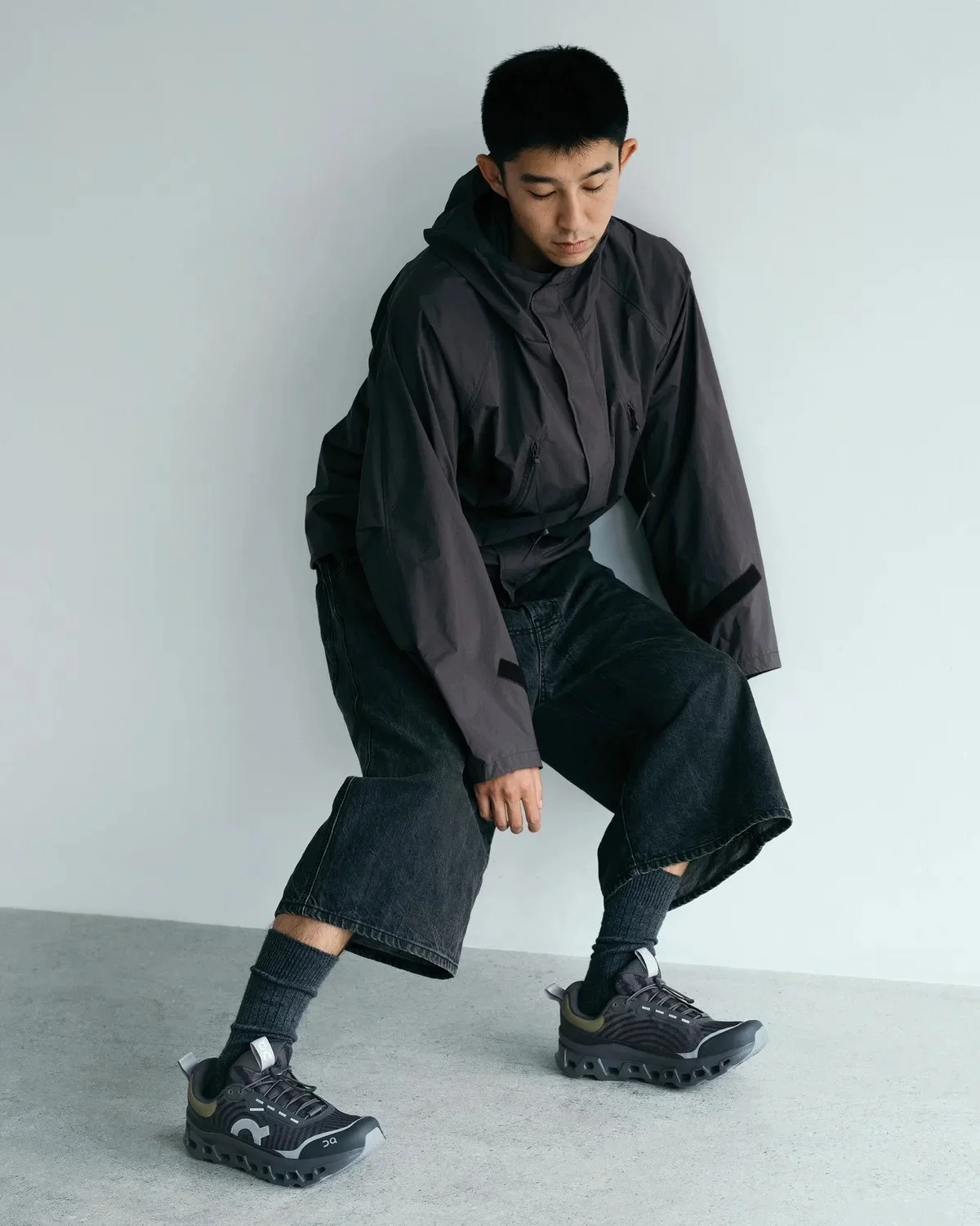 Dark grey hooded jacket, black cropped jeans, and dark grey On running sneakers.