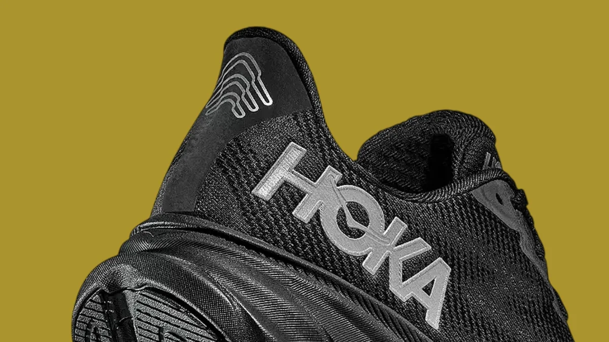 Close-up of a black Hoka running shoe heel, featuring reflective silver branding and a graphic logo on the collar.