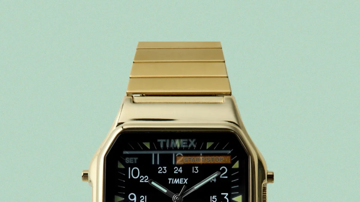 Gold-toned Timex digital-analog watch with black face and metal link band on a light green background.