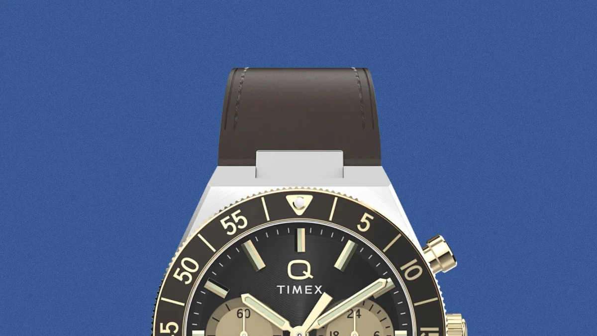 Black and gold Timex Q chronograph watch with brown leather strap against blue background.