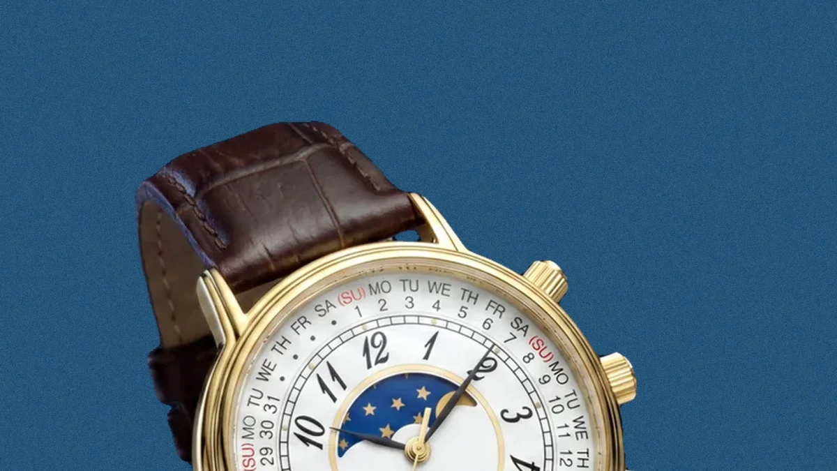 Gold wristwatch with white dial, moon phase indicator, black numerals, and brown leather strap on blue background.