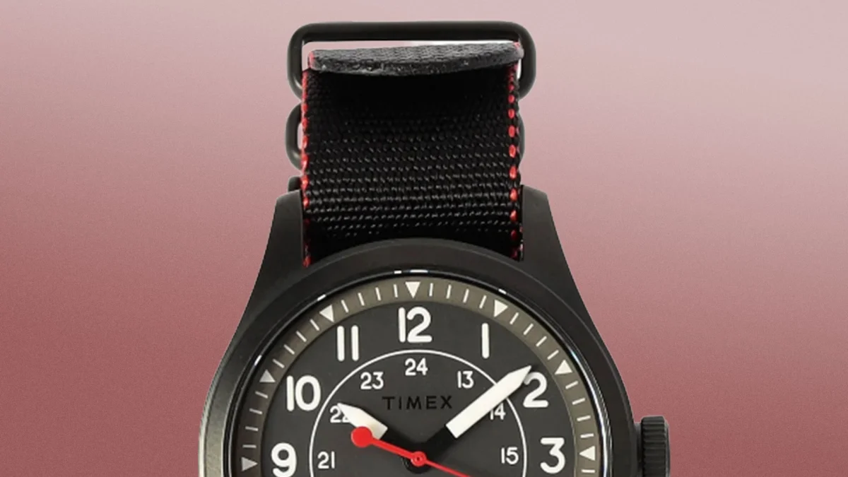 Black Timex wristwatch with white numerals and red second hand on a black fabric strap with red stitching.