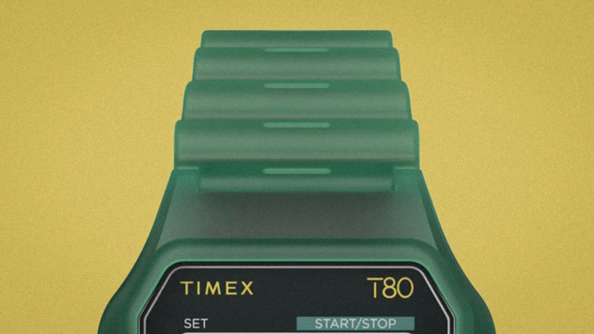 Green Timex T80 digital watch with segmented strap on a yellow background.