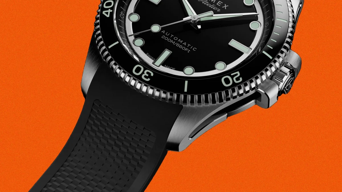 Close-up of a black dive watch with luminous markers, a rotating bezel, and a textured black rubber strap on an orange background.