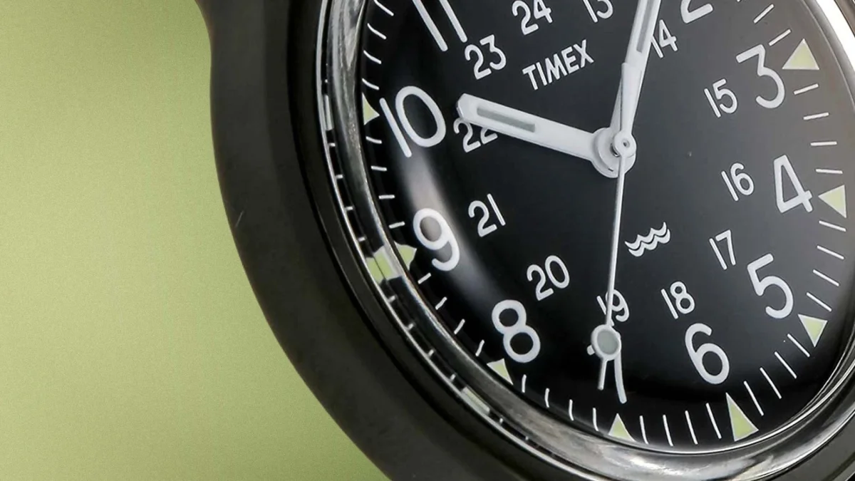 Close-up of a black Timex watch face with white numerals and hands showing the time at 10:03:35.