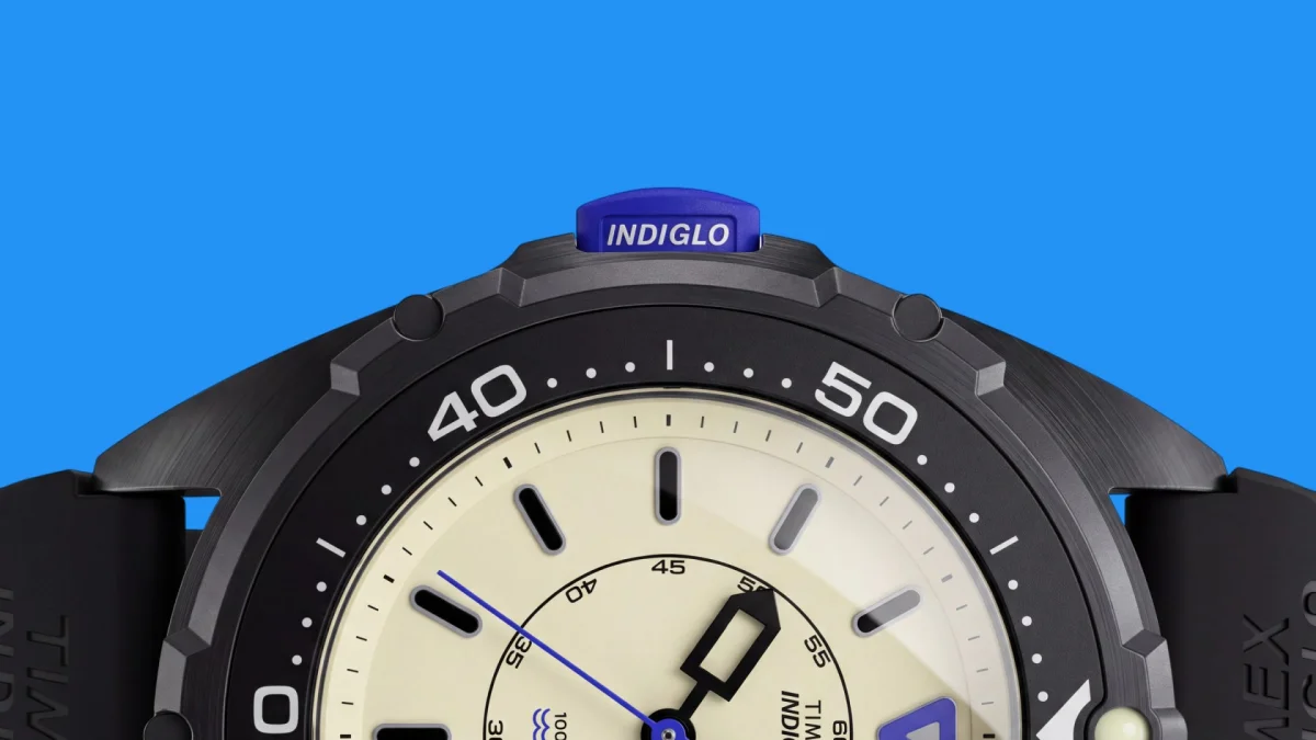 Close-up of a Timex watch with a cream-colored dial, a black rotating bezel, and a blue Indiglo button at the top of the case.
