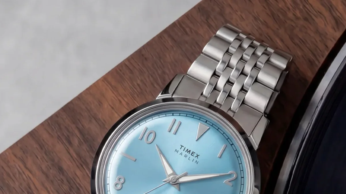 Silver Timex Marlin watch with blue face and metal band, partially visible resting on a wooden surface.