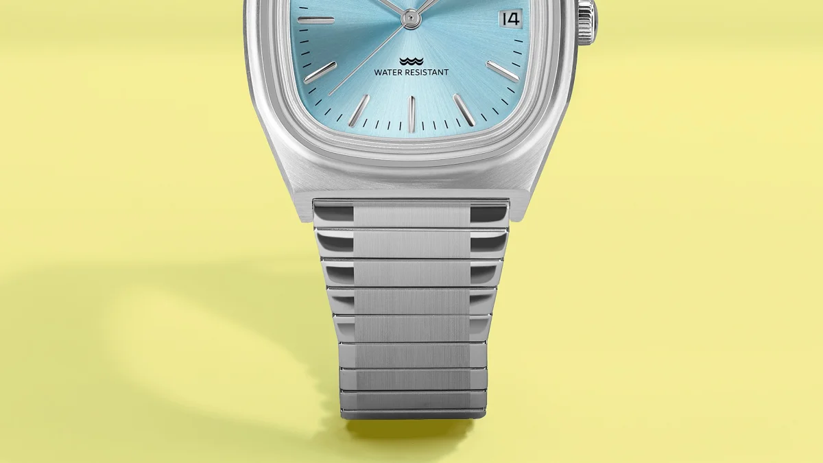 Silver metal wristwatch with a light blue dial and date display on a yellow background.