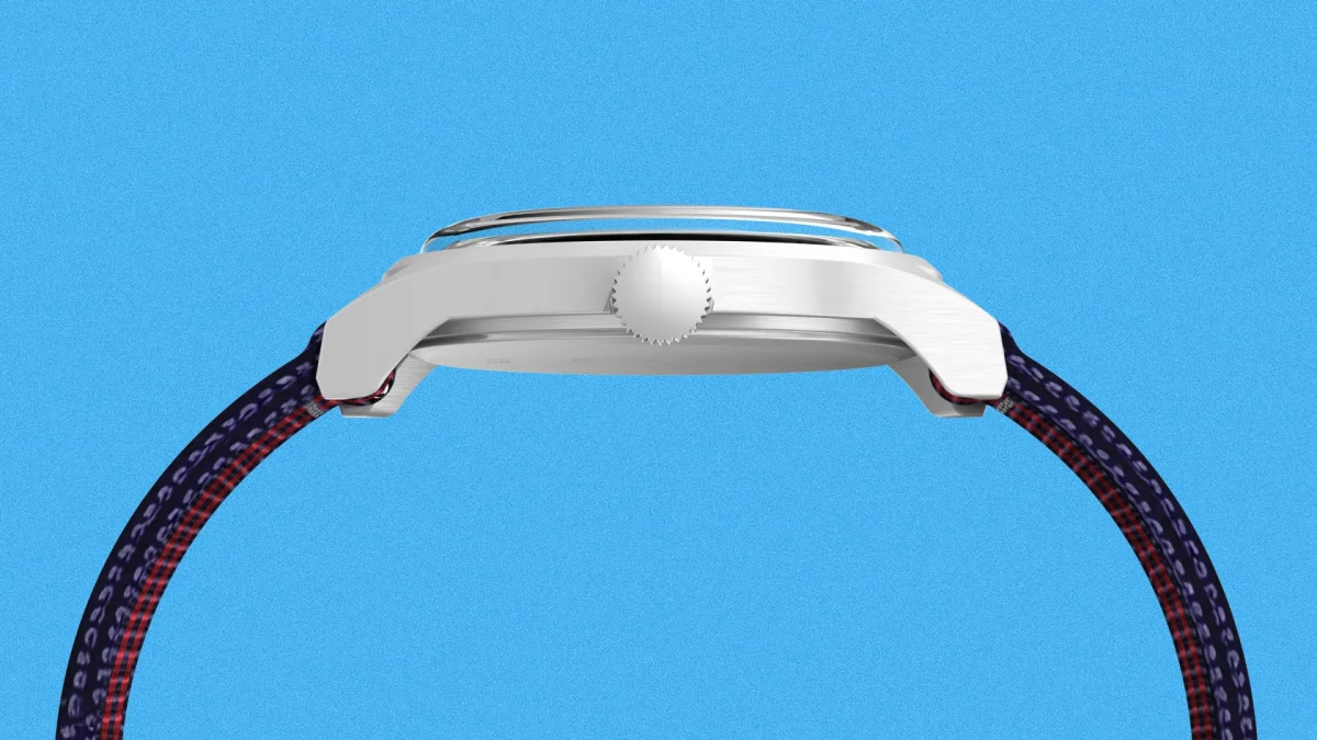 Side view of a silver metal watch case with a ridged crown and a blue and red patterned fabric strap.