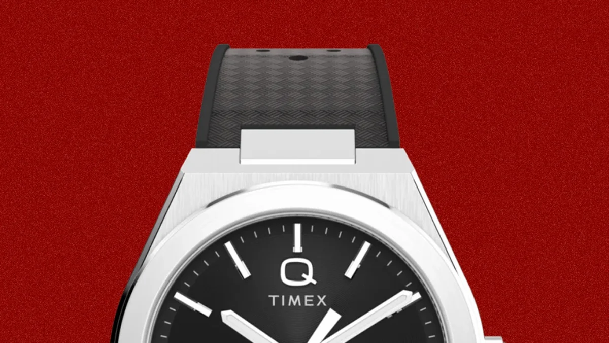 Silver Timex Q watch with black dial and black textured rubber strap on a red background.