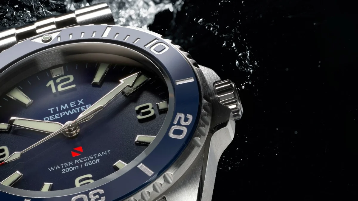 Close-up of a Timex Deepwater watch with a blue bezel, silver case, and water droplets in the background.