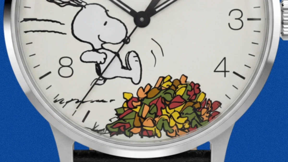 Close-up of a watch face featuring Snoopy kicking a colorful pile of leaves near the 8 and 4 o'clock markers.