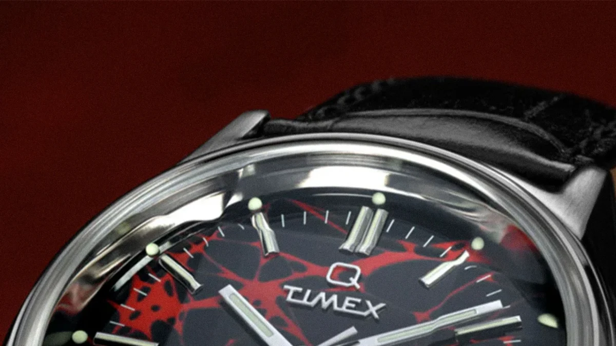 Close-up of a Timex watch face with a black and red abstract pattern and silver hour markers, attached to a black leather strap.