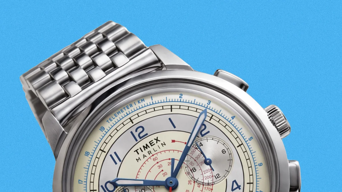 Silver Timex Marlin watch with a metal link band, white dial, and blue, red, and black markings on the face, shown in close-up against a bright blue background.